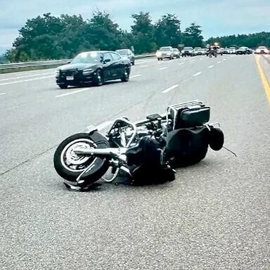 A motorcycle lies on its side in the middle of a highway, with cars visible in the background.