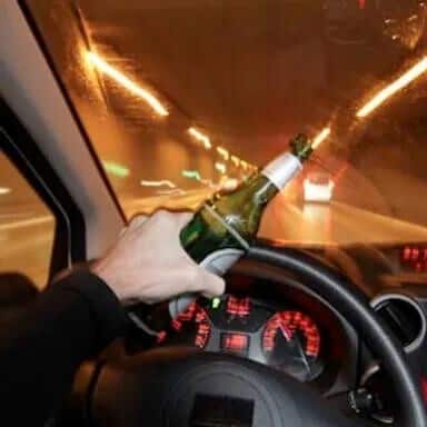 A person is holding a bottle of beer while driving through a tunnel at night.