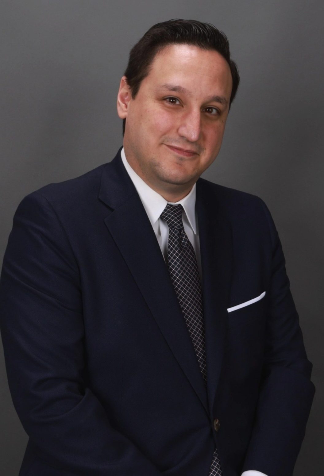 David Gutierrez, Litigation Attorney at Law. A man in a navy suit and tie stands in front of a plain gray background, looking at the camera with a slight smile.